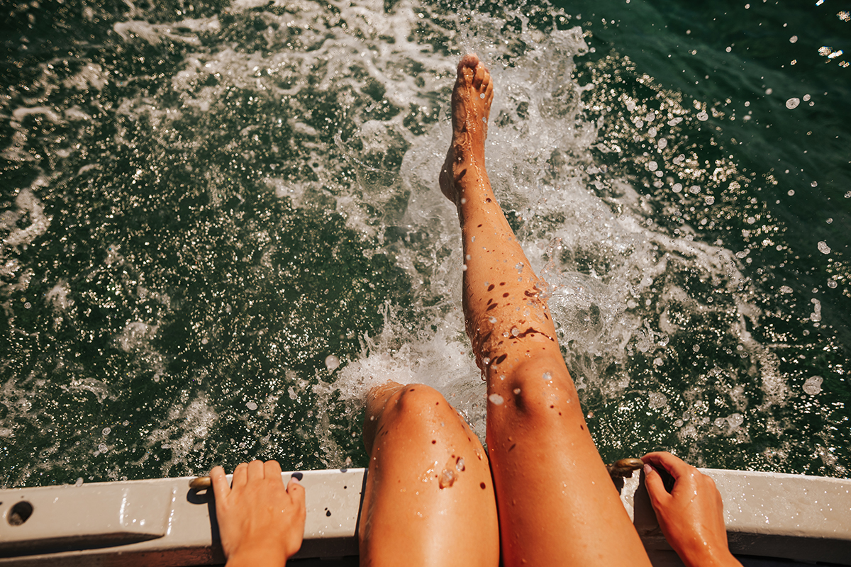 A woman is sitting on the deck of a boat, splashing her feet in the water