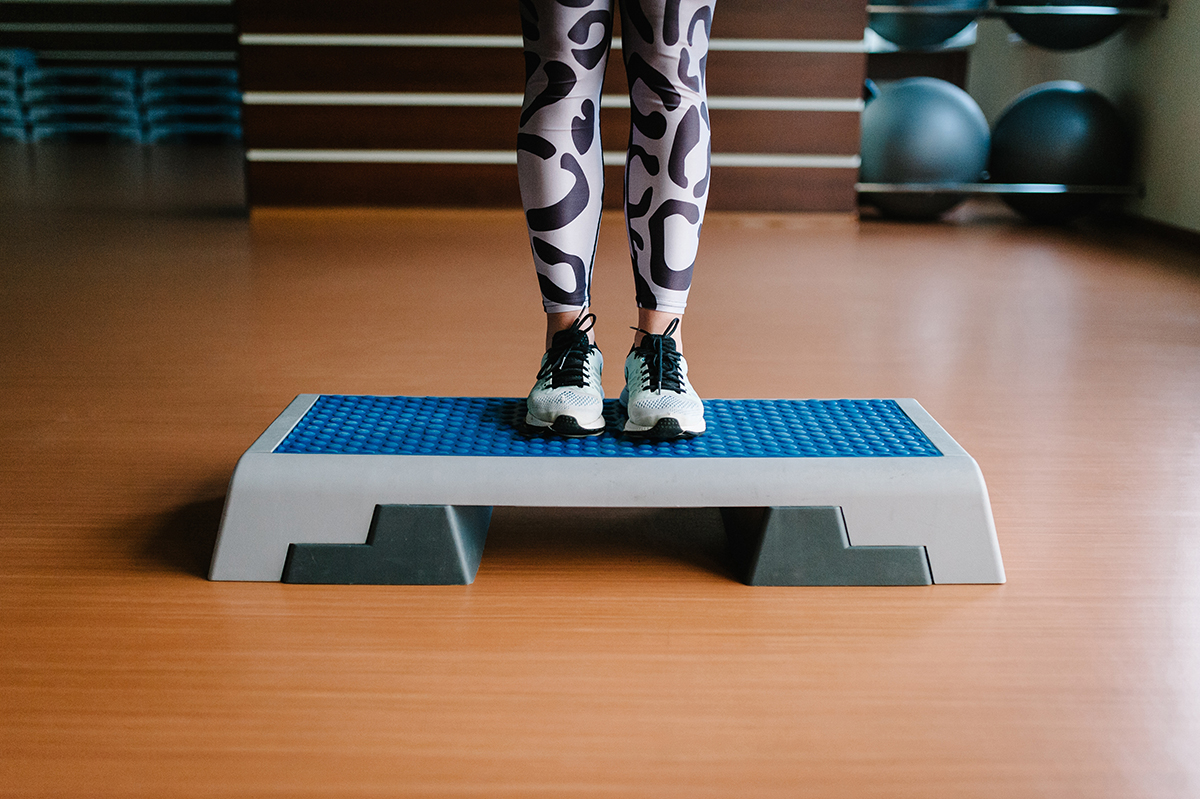 A woman wearing patterned gym leggings is standing on a step platform
