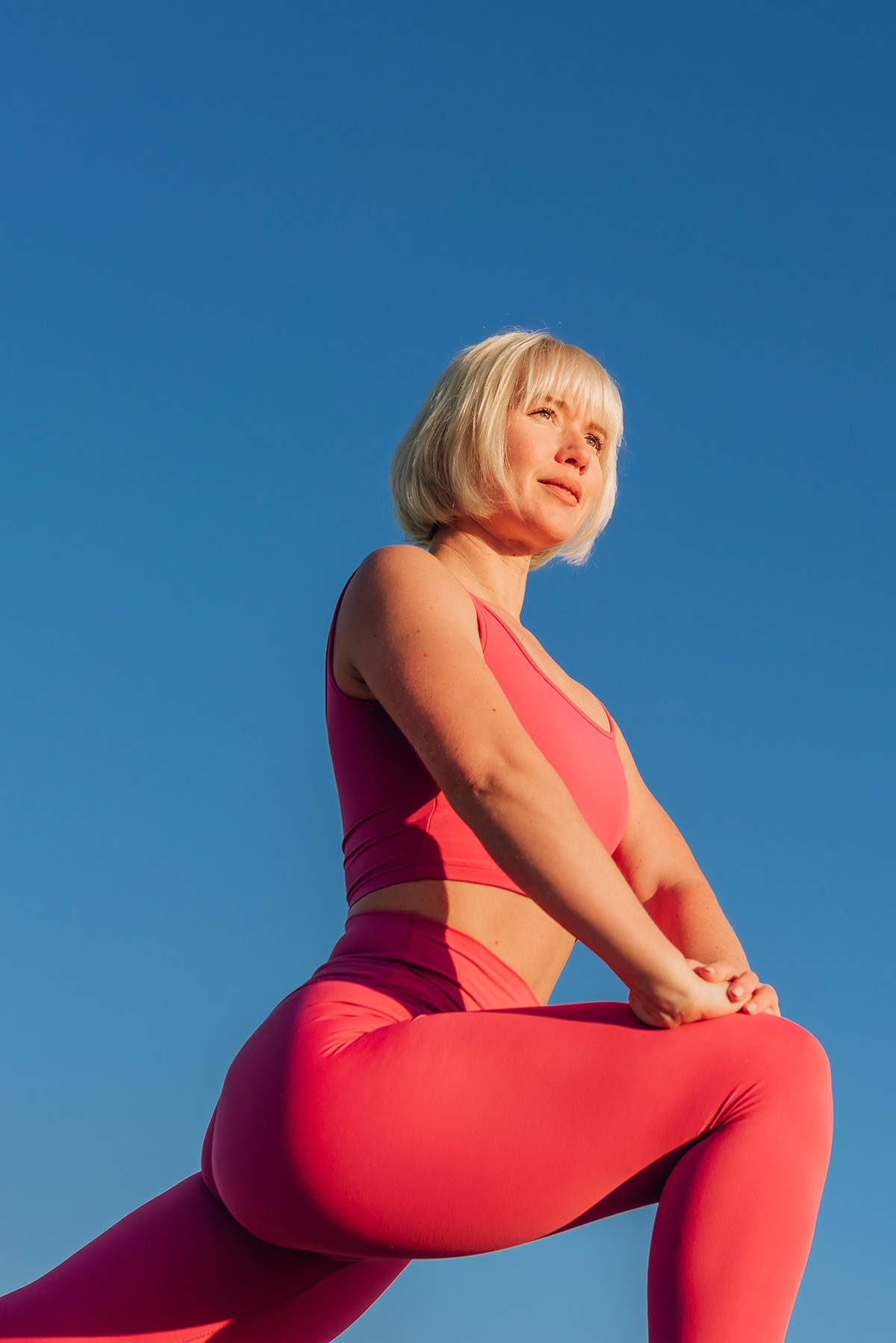 A woman wearing a gym set is doing a lunge stretch against a blue background