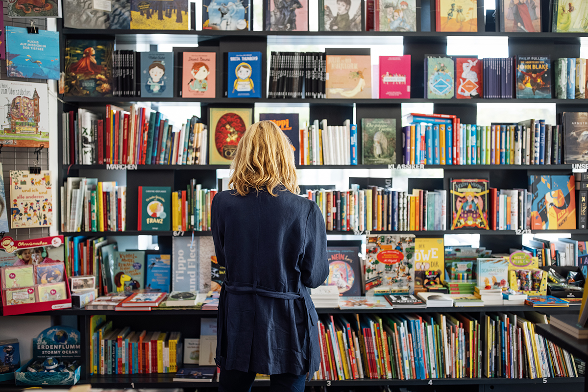 A woman stands in front of shelves of books in a bookshop with her back to the camera.