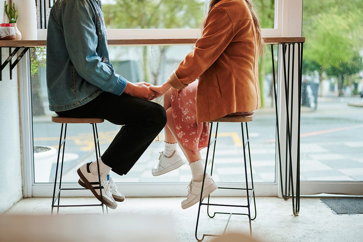 A couple sitting on stools holding hands in a cafe.