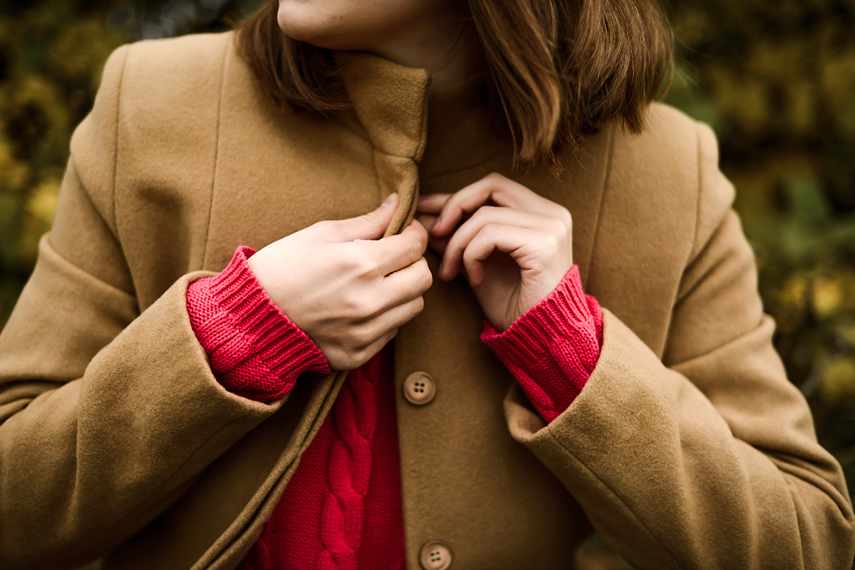 A woman buttons up a light brown coat.