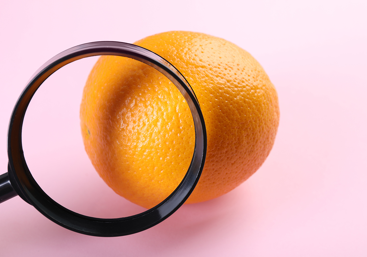 A magnifying glass is positioned in front an orange against a pink background.