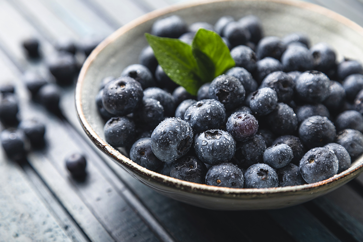 A bowl containing blueberries sits on a wooden surface.