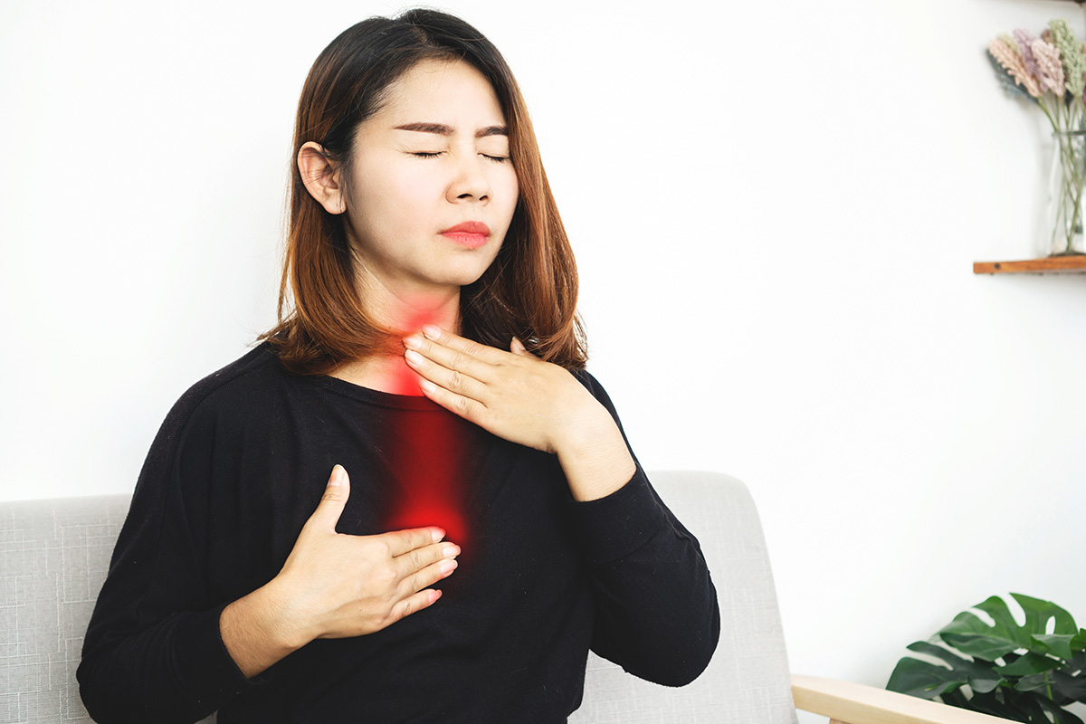 A woman touches her throat and chest, with the area highlighted in red to illustrate heartburn