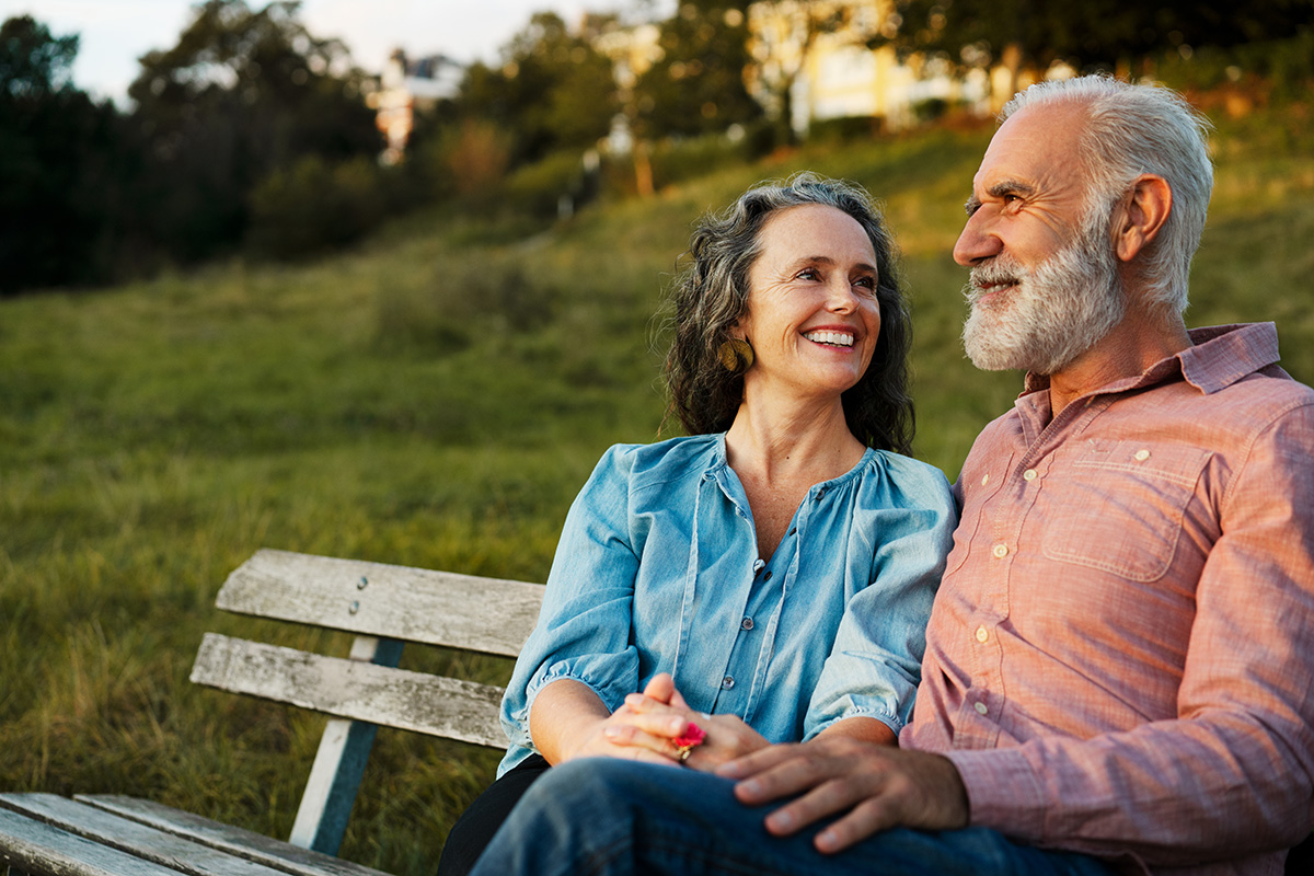 A man and woman are sitting on a bench outside, smiling