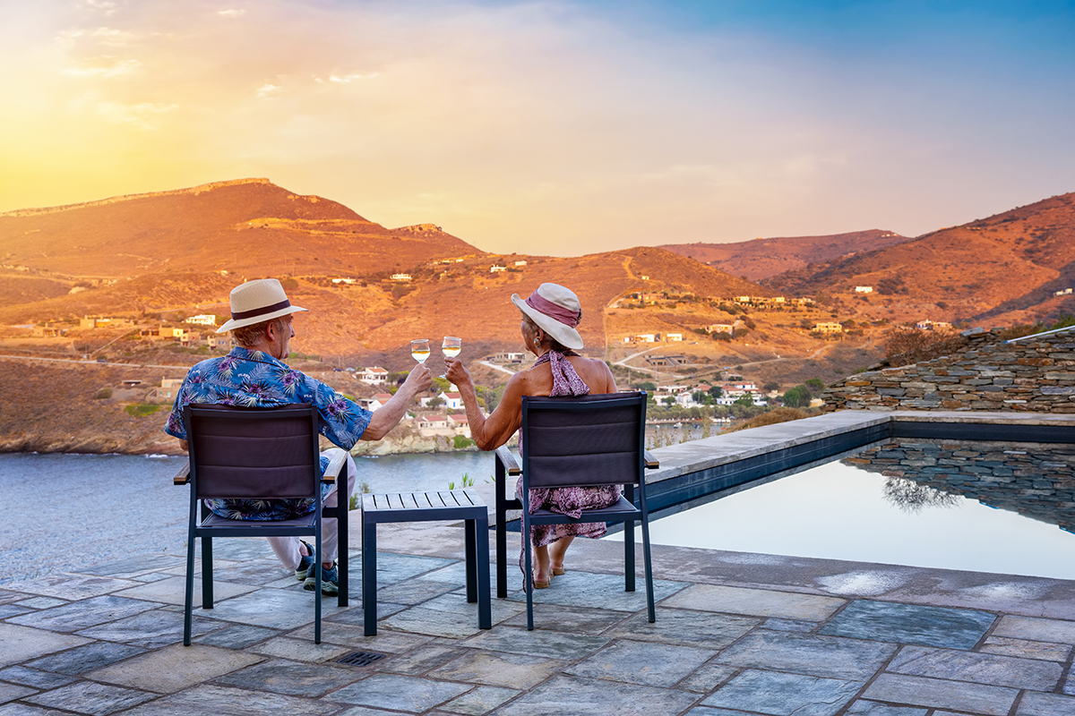 An elderly couple sitting by a pool at sunset, clinking glasses