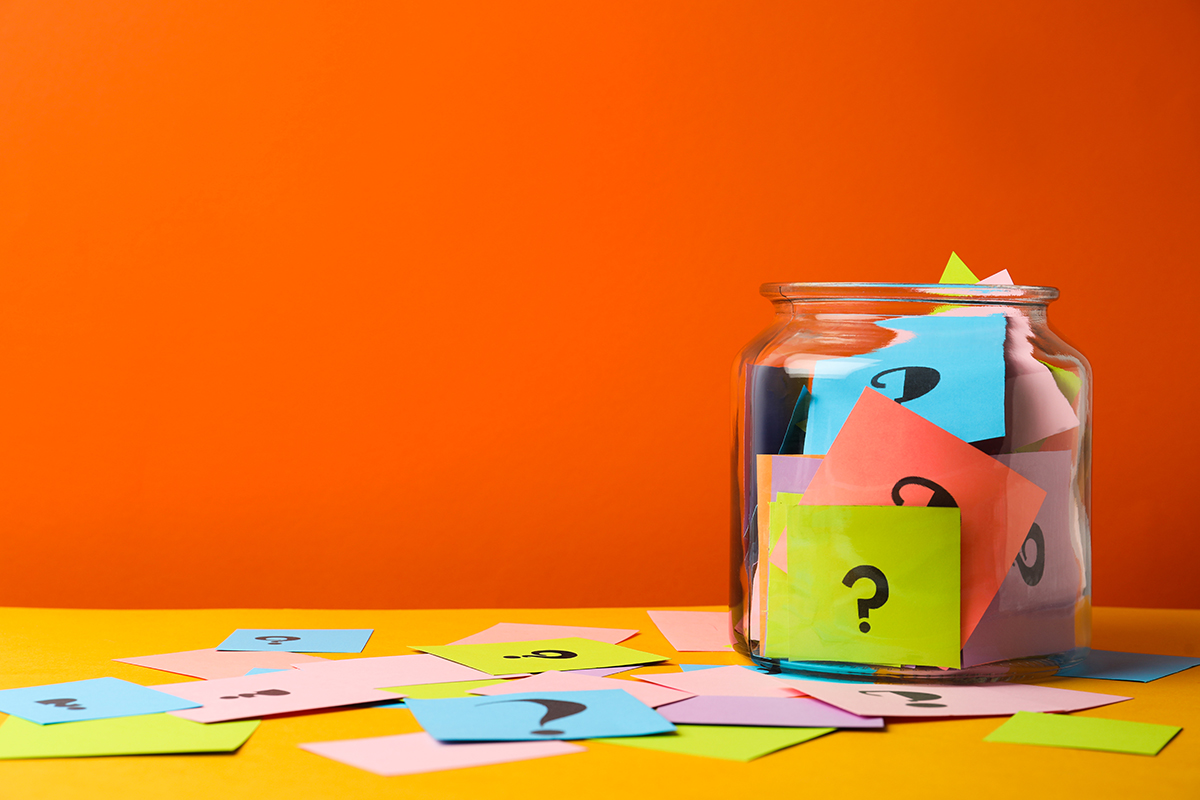 A glass jar containing colourful cards with question marks against an orange background