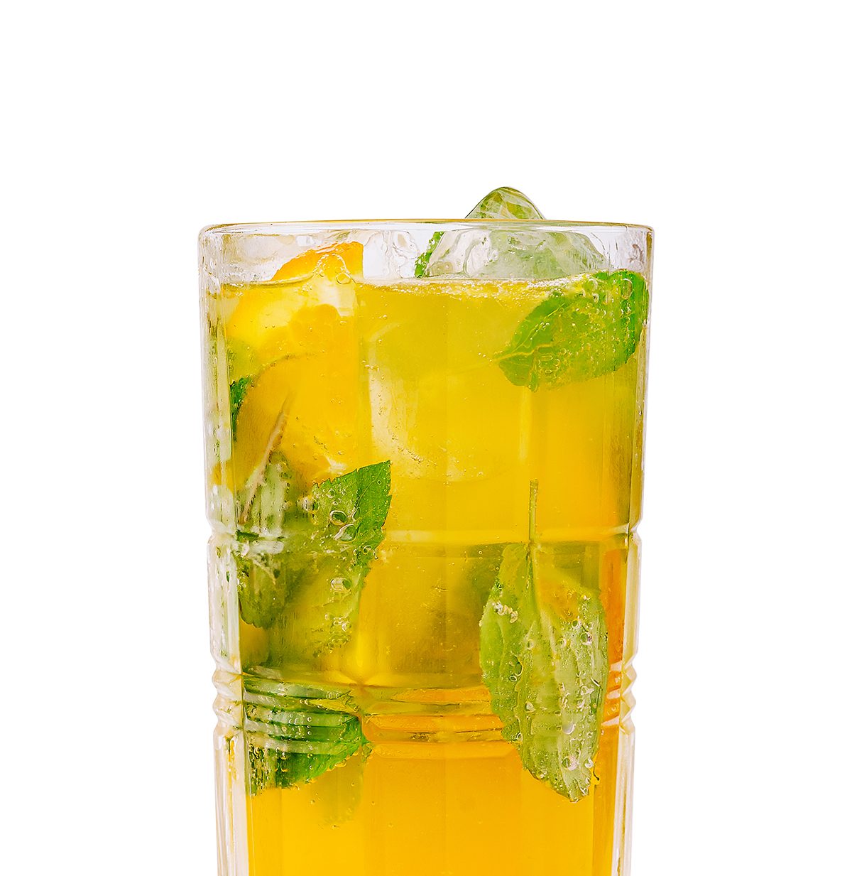 A glass filled with a yellow liquid, mint and ice against a white background