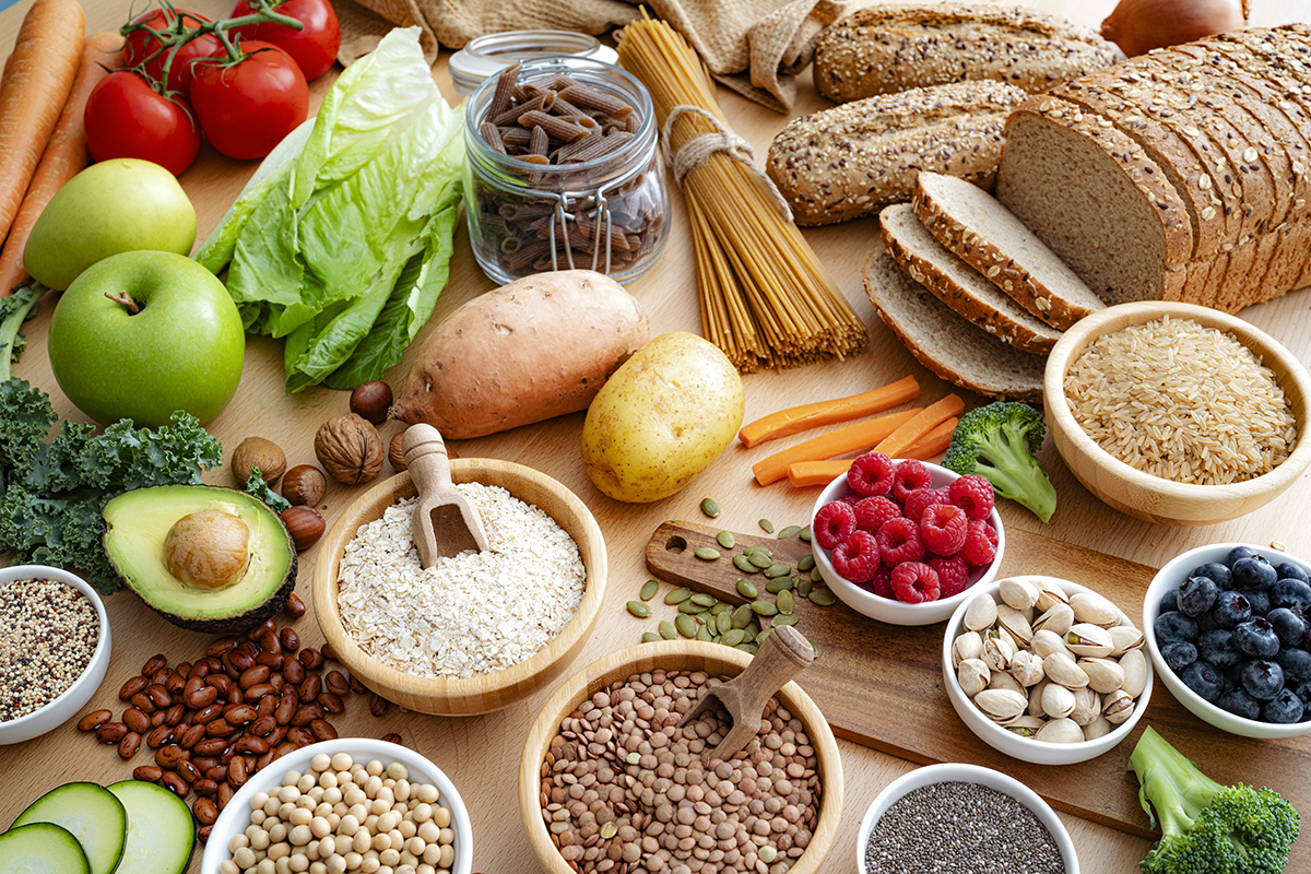 An assortment of healthy, high-fibre foods, including fruits, vegetables, whole grains and nuts, sit on a wooden surface