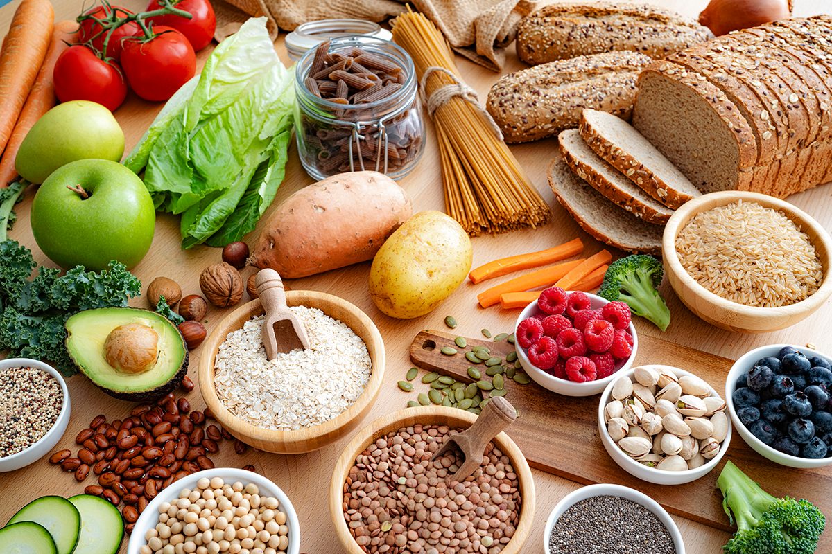 An assortment of healthy, high-fibre foods, including fruits, vegetables, whole grains and nuts, sit on a wooden surface