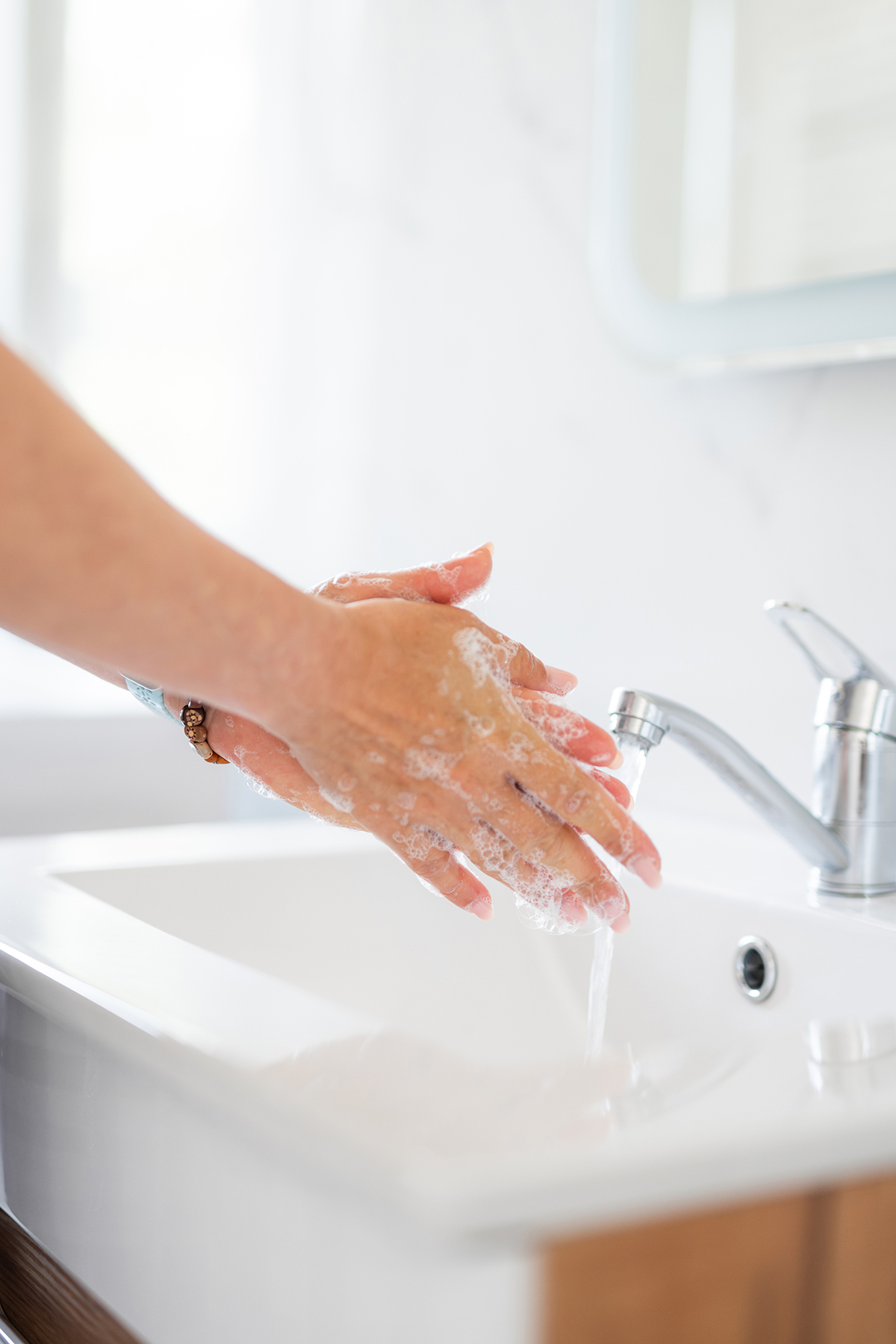 A close up of a woman washing her hands in a bathroom sink.