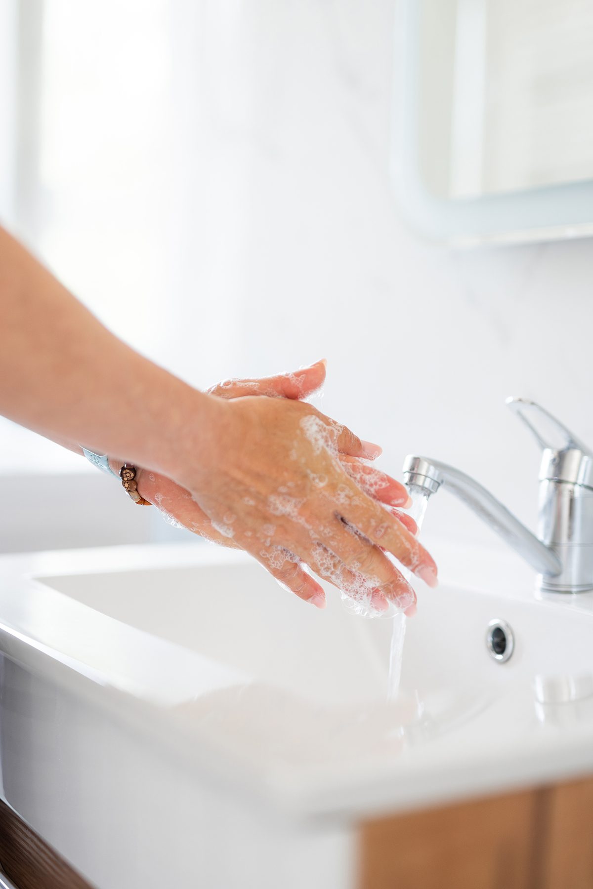 A close up of a woman washing her hands in a bathroom sink.