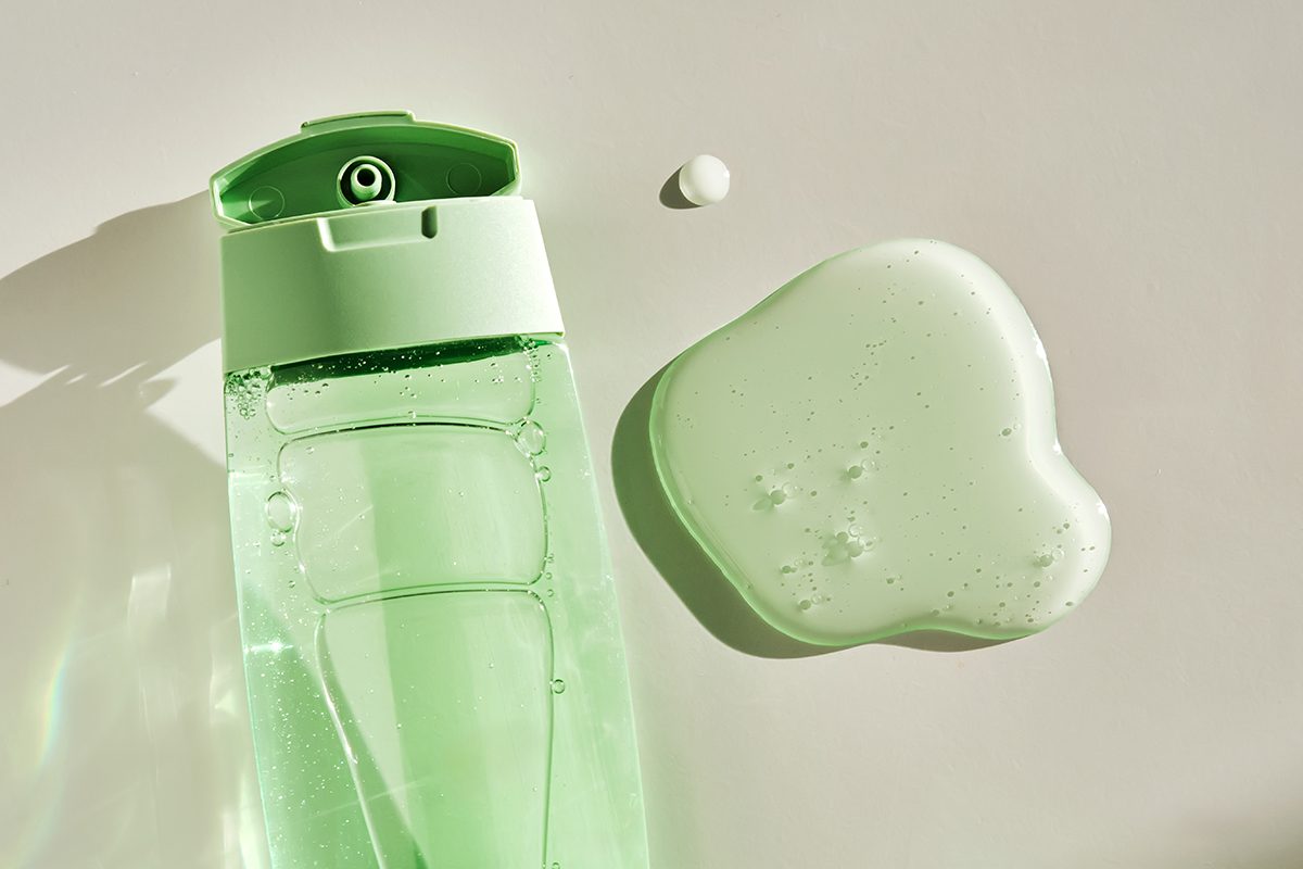 A shower gel or shampoo bottle and a blob of the product are on a white background.