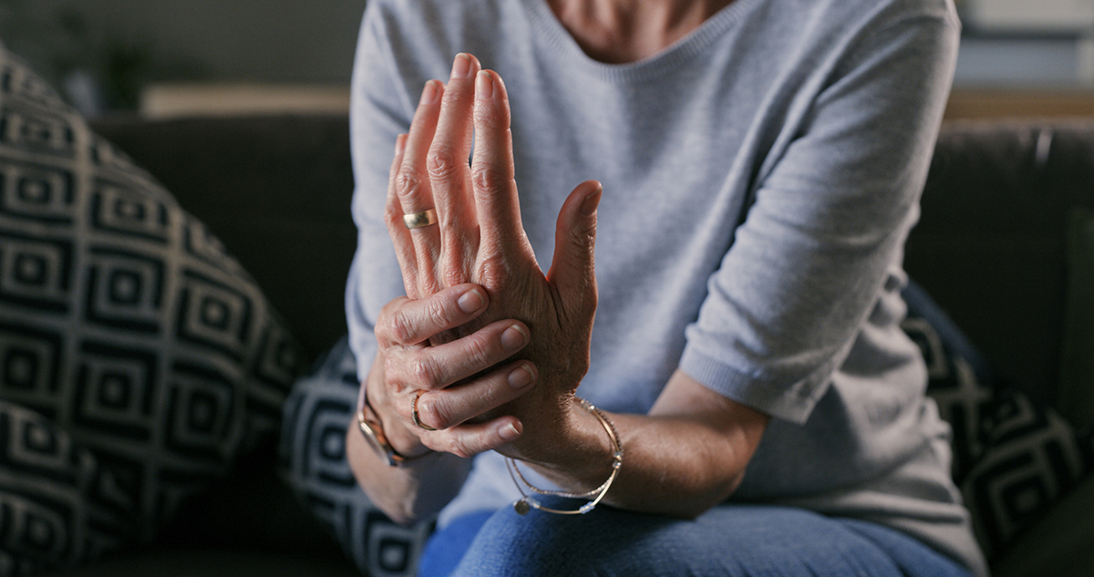 A senior woman is sitting on a sofa, holding her hand