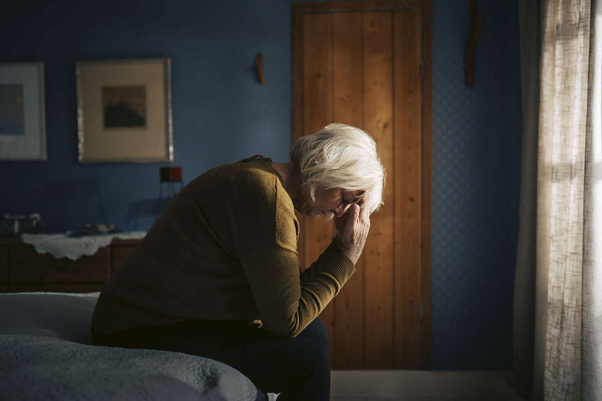 A woman is sitting on the edge of a bed, with her head in her hands