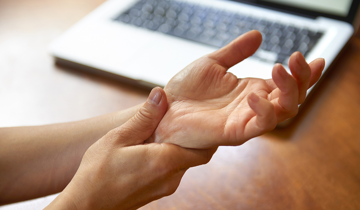 A person is holding their wrist next to a laptop