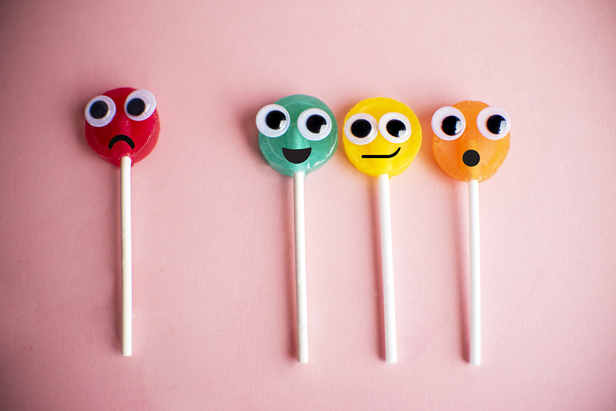 Four colourful lollipops with googly eyes and different facial expressions on a pink background