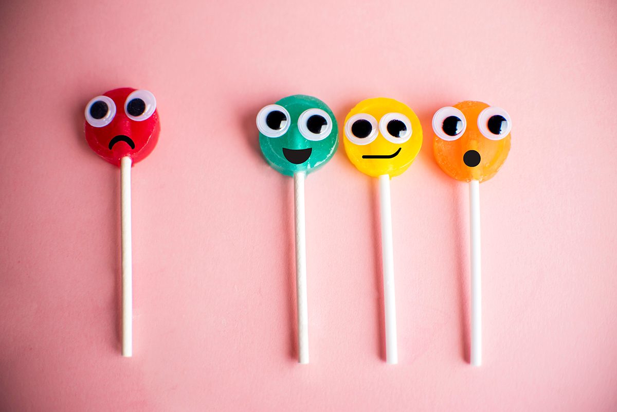 Four colourful lollipops with googly eyes and different facial expressions on a pink background