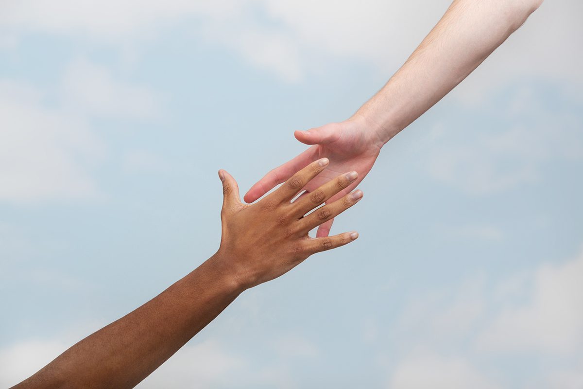 Two hands reaching out to touch against a cloudy sky