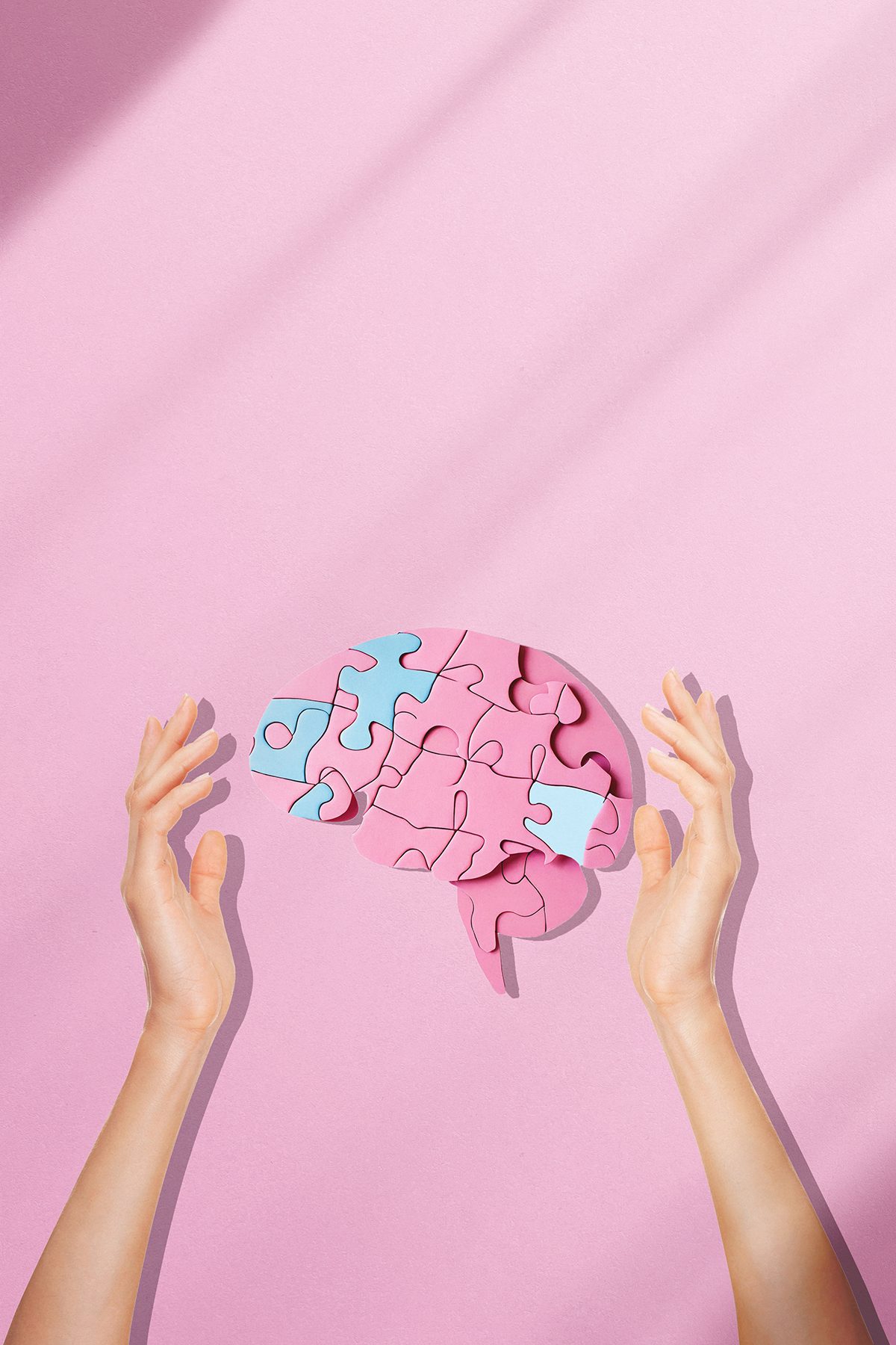 A brain made from jigsaw pieces between two hands on a pink background