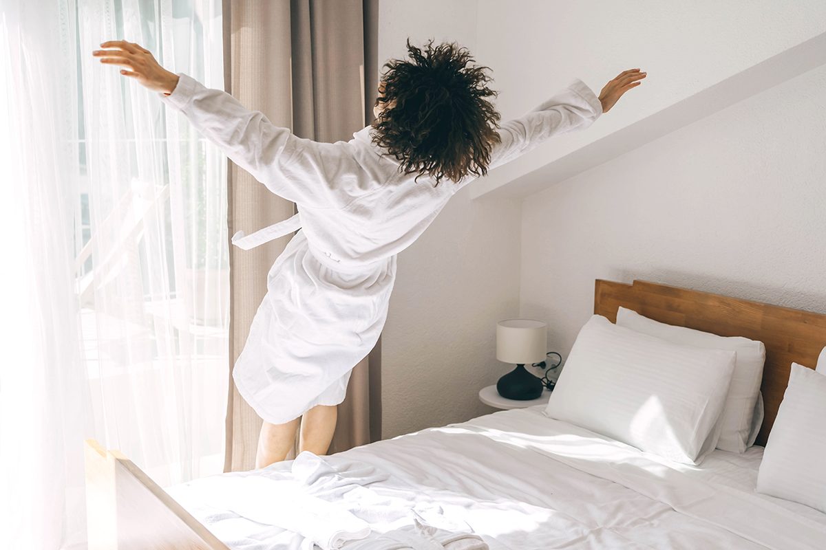 A woman in a white robe is falling onto a bed in a hotel.