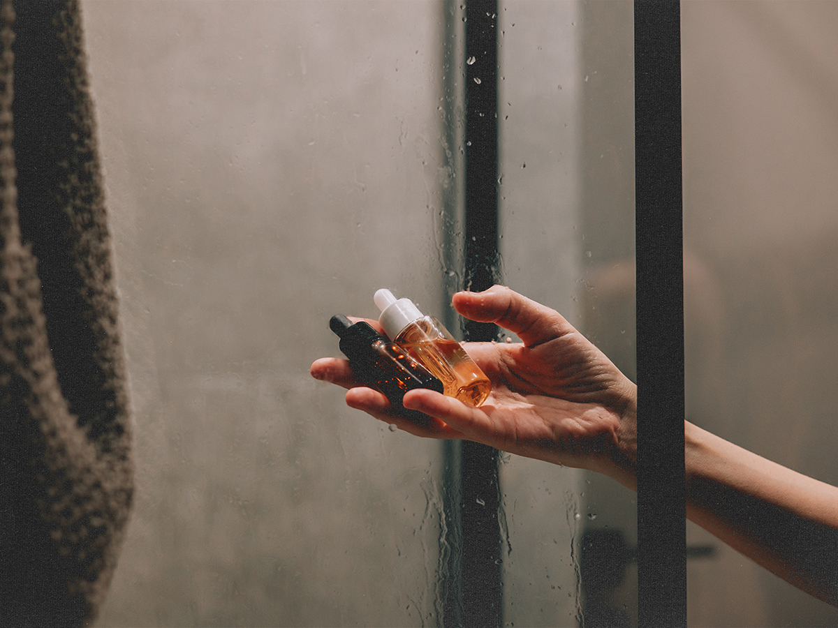 Female hand holding skincare serums in a steamy shower.