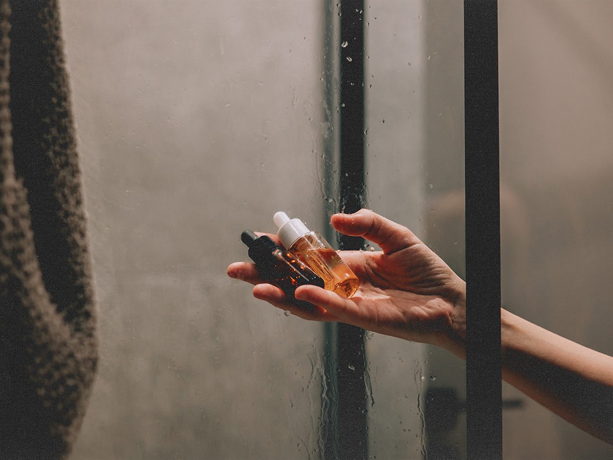 Female hand holding skincare serums in a steamy shower.