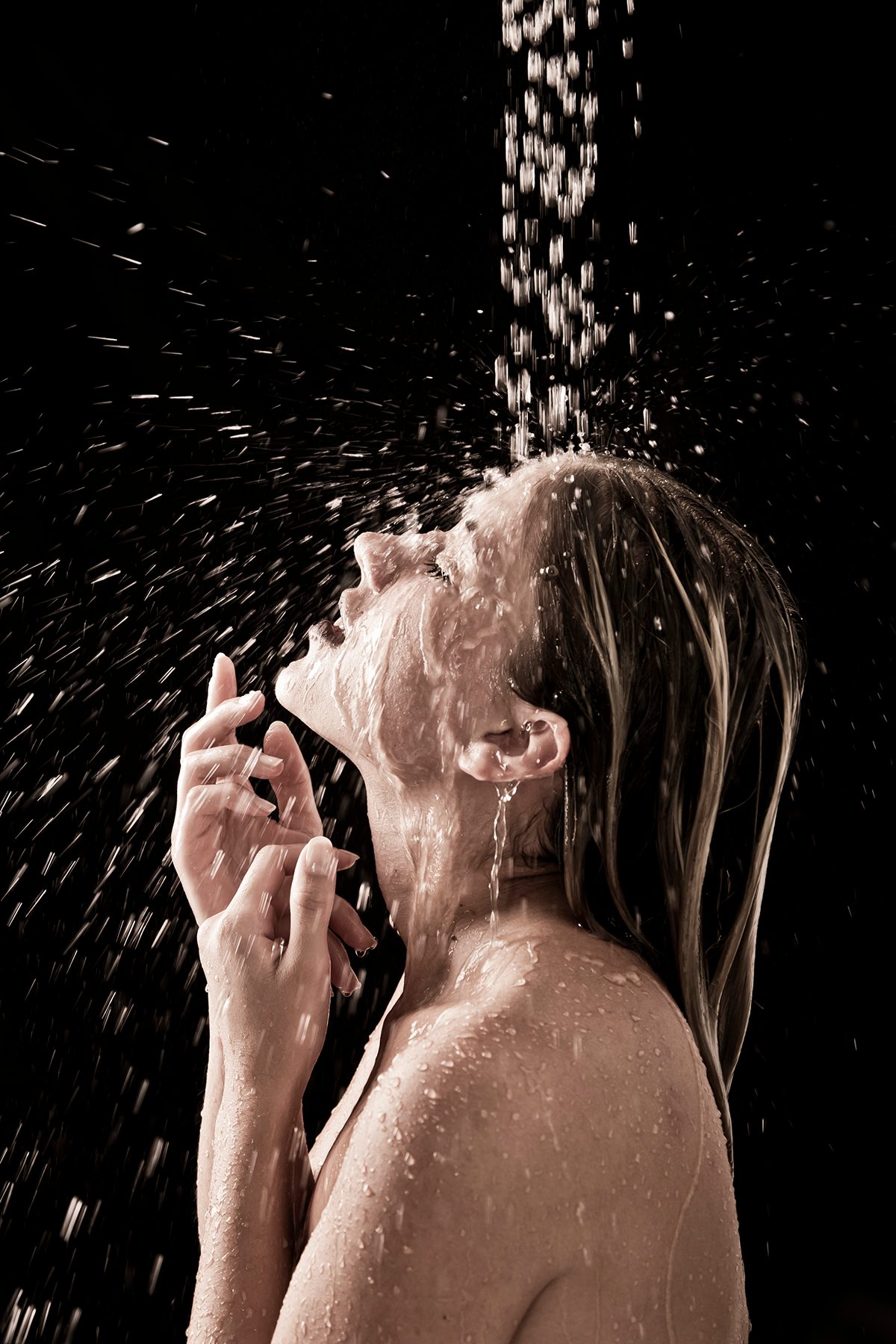 A woman is under a rainfall shower with a black backdrop.