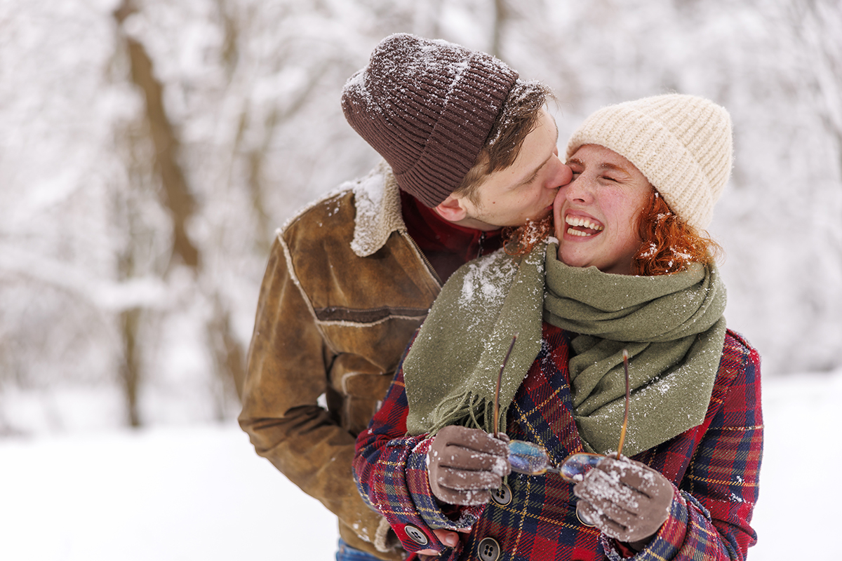 A man kissing his partner on the cheek outside in the snow