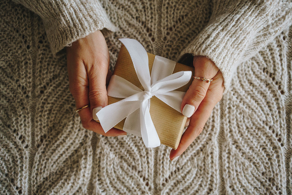 An overhead shot of female hands holding a gift, wrapped in brown paper and a bow
