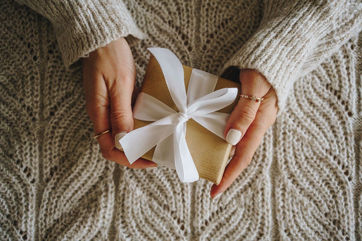 An overhead shot of female hands holding a gift, wrapped in brown paper and a bow