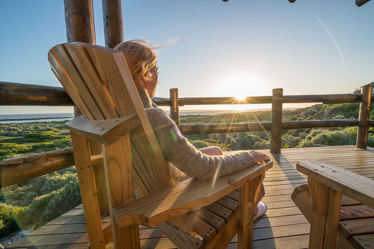 A woman sitting on a wooden chair on a terrace at sunset