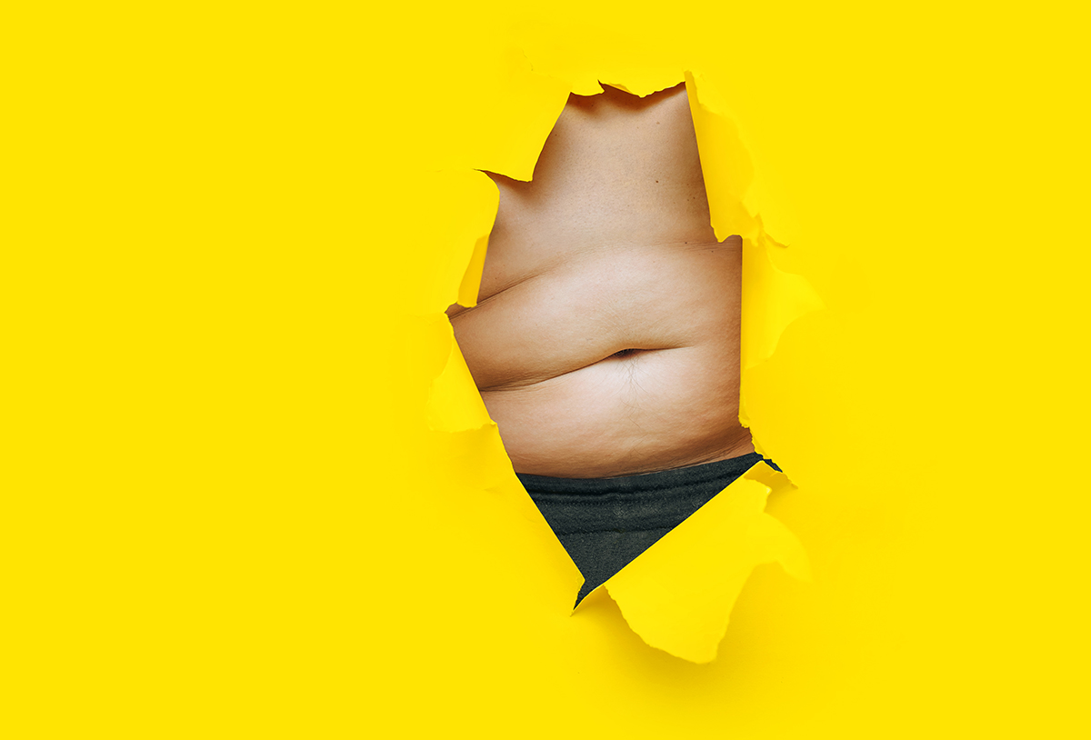 A stomach is visible through a hole in a sheet of torn yellow paper