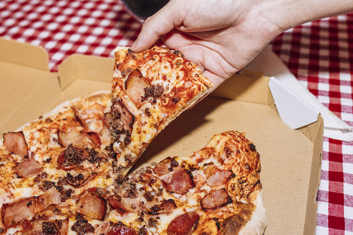 A hand taking a slice of pizza from a pizza box