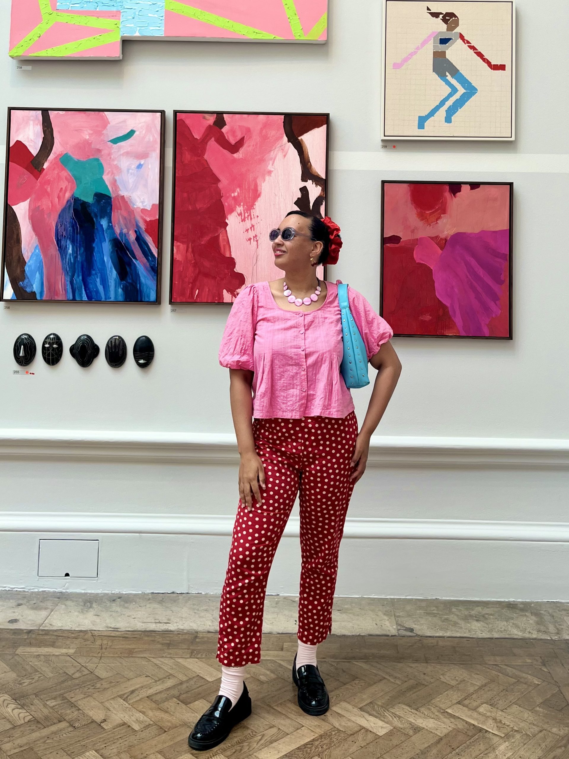 Woman dressed in colourful outfit stood in front of paintings.