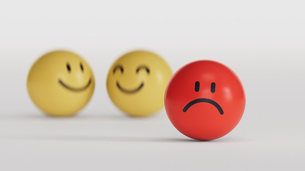 A round red ball with a sad face drawn on it, positioned in the foreground, with two yellow balls with happy faces in the background