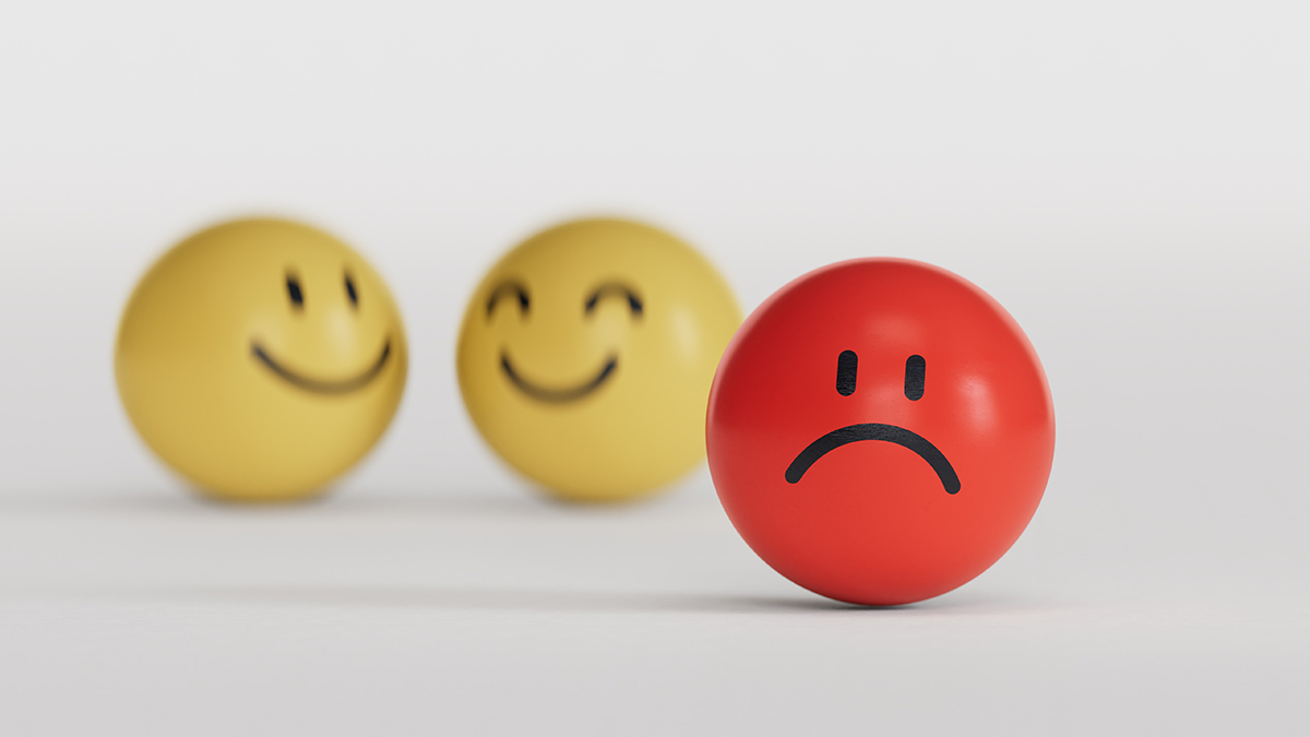 A round red ball with a sad face drawn on it, positioned in the foreground, with two yellow balls with happy faces in the background