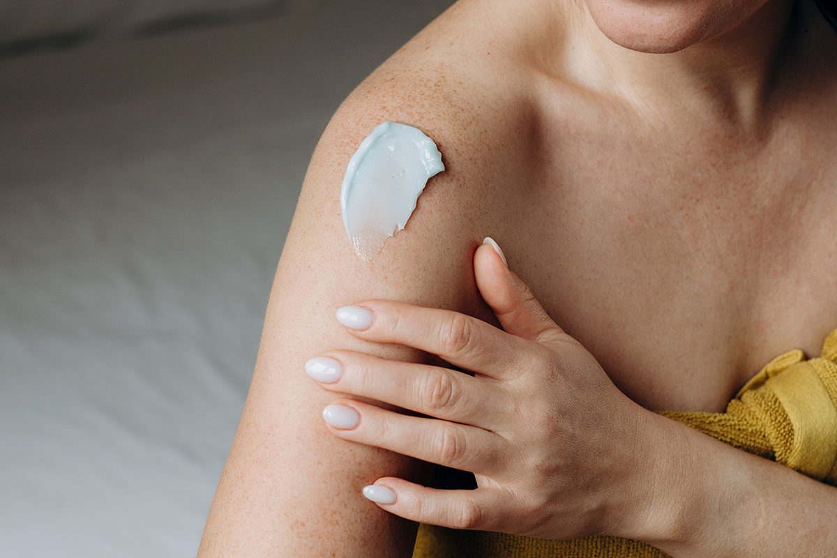 A close-up of a woman applying cream to her body