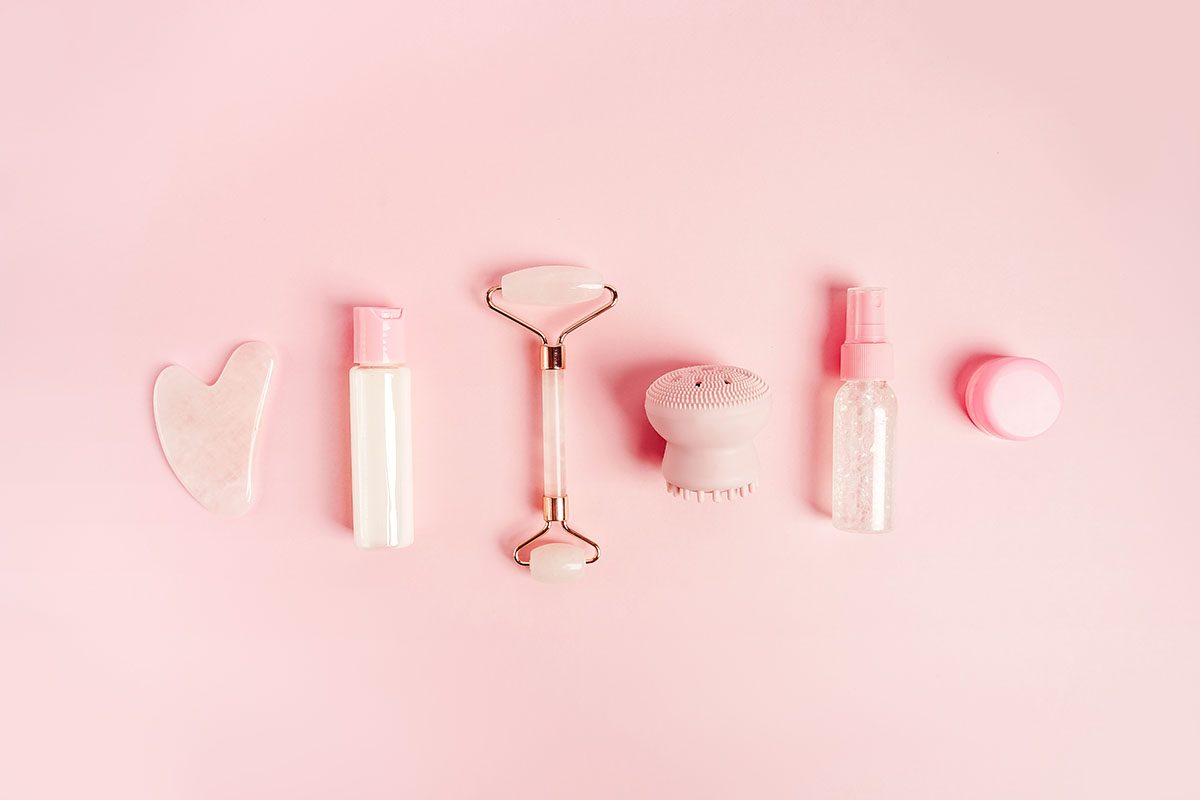 A range of skincare products and tools on a pink background
