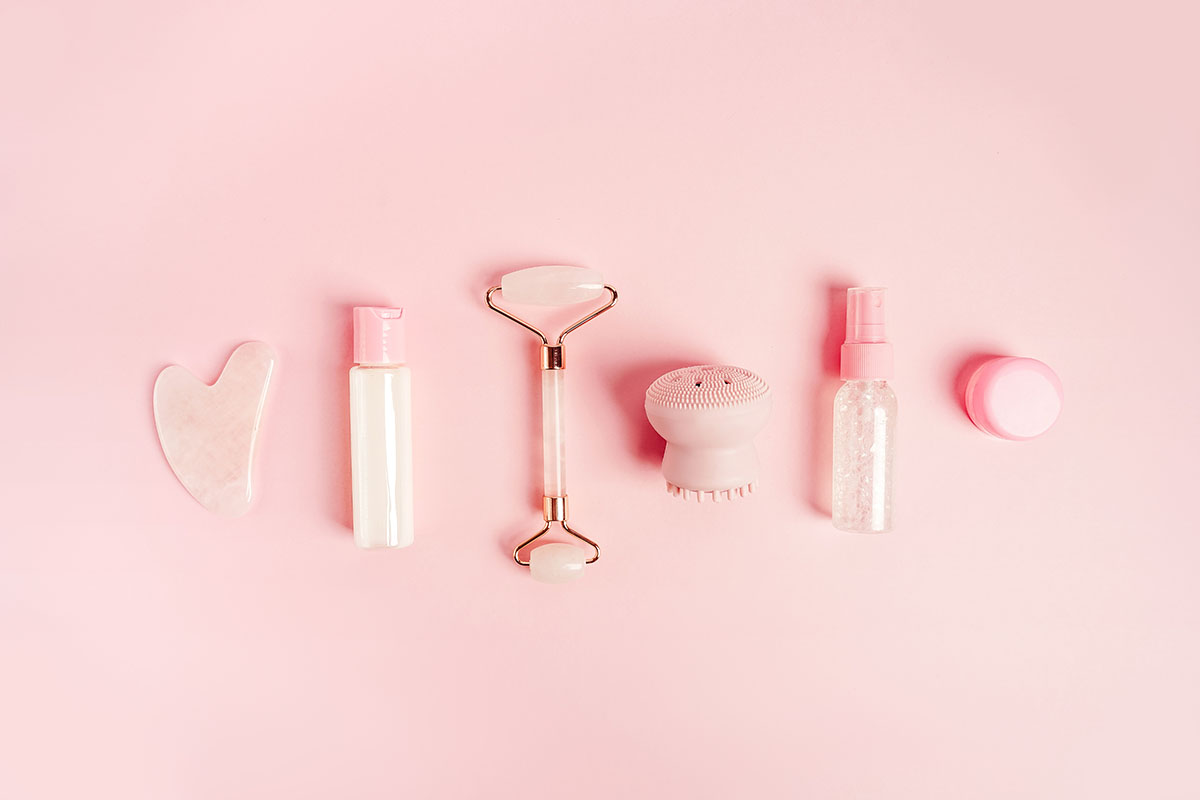 A range of skincare products and tools on a pink background