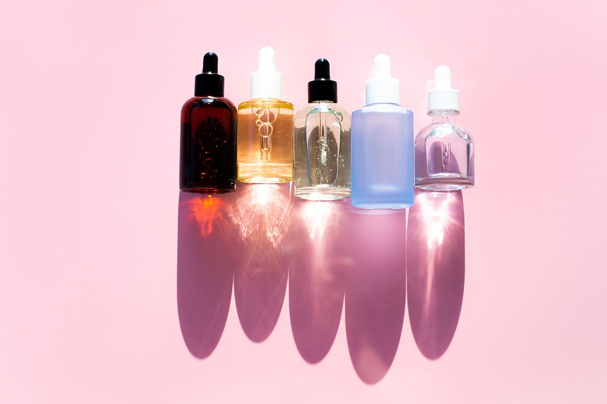 Five cosmetic bottles are arranged in a row on a pink background