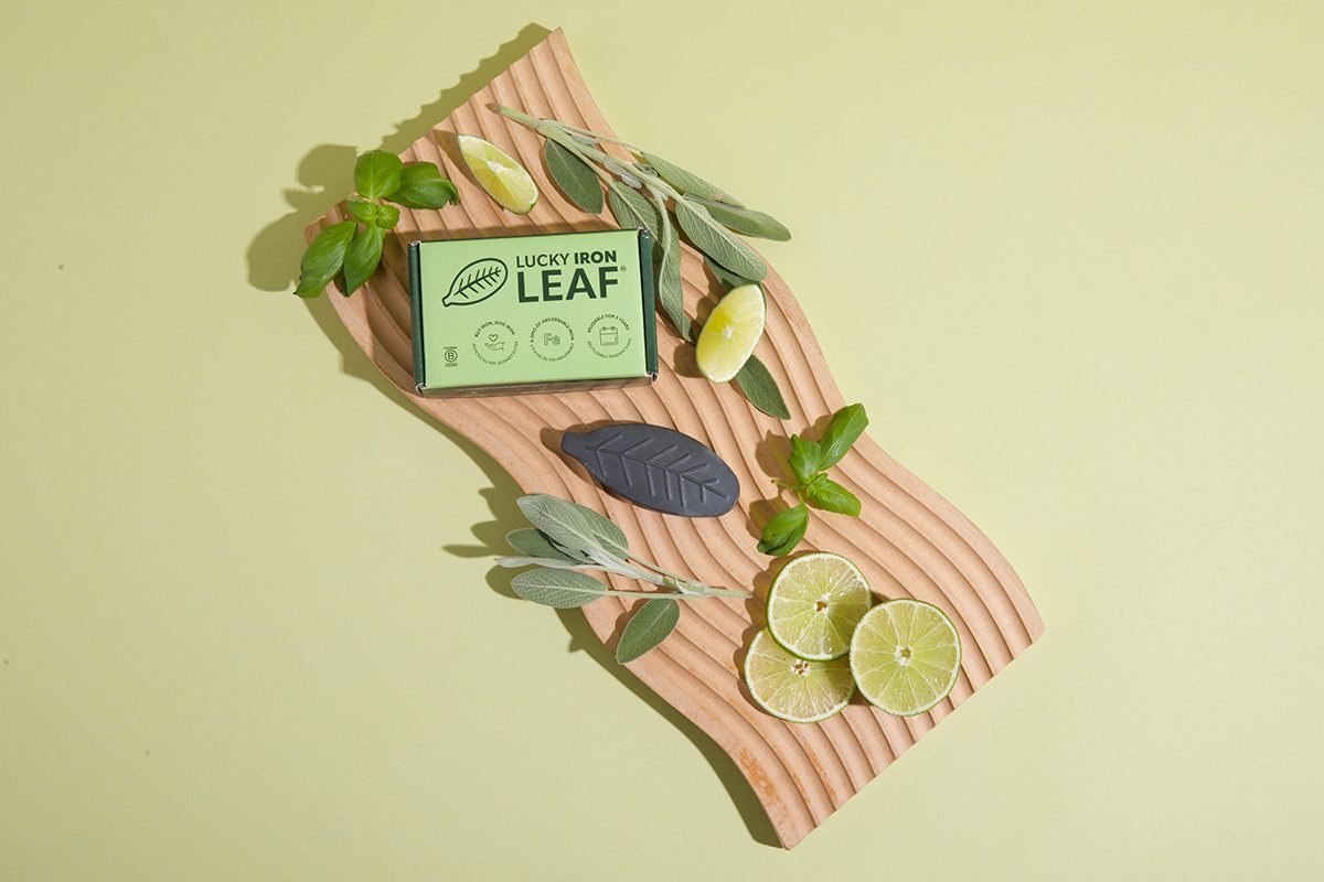 The Lucky Iron Leaf cooking tool sits on a wooden board, surrounded by leaves and lime slices, against a green background