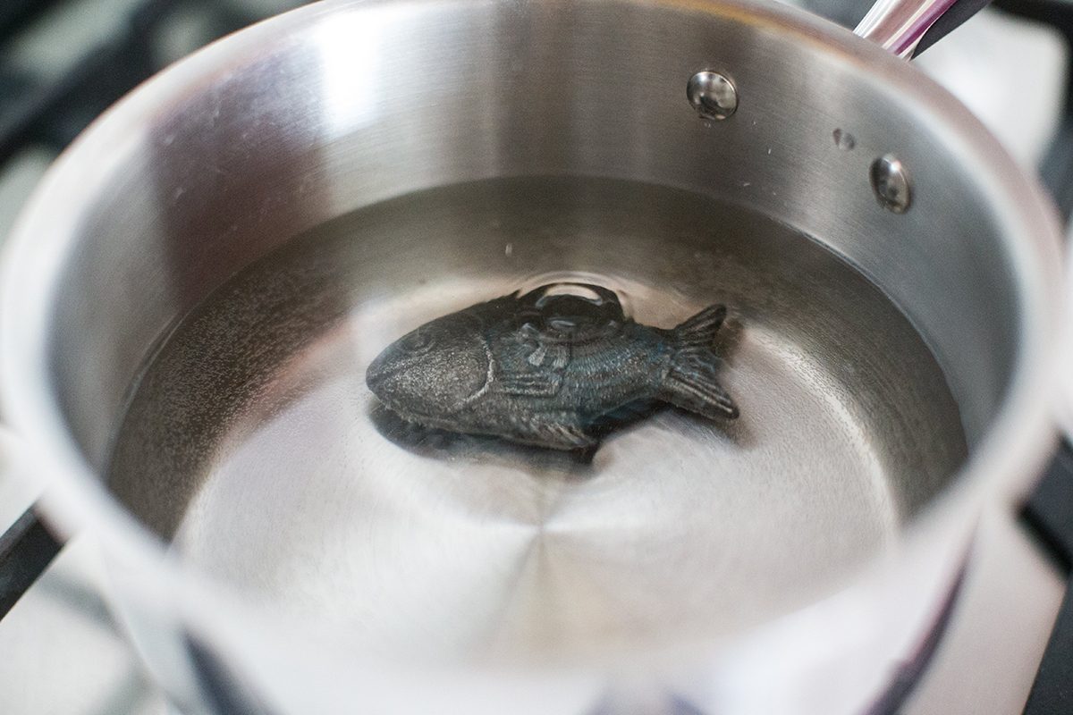 A metal saucepan containing water and a cast-iron fish