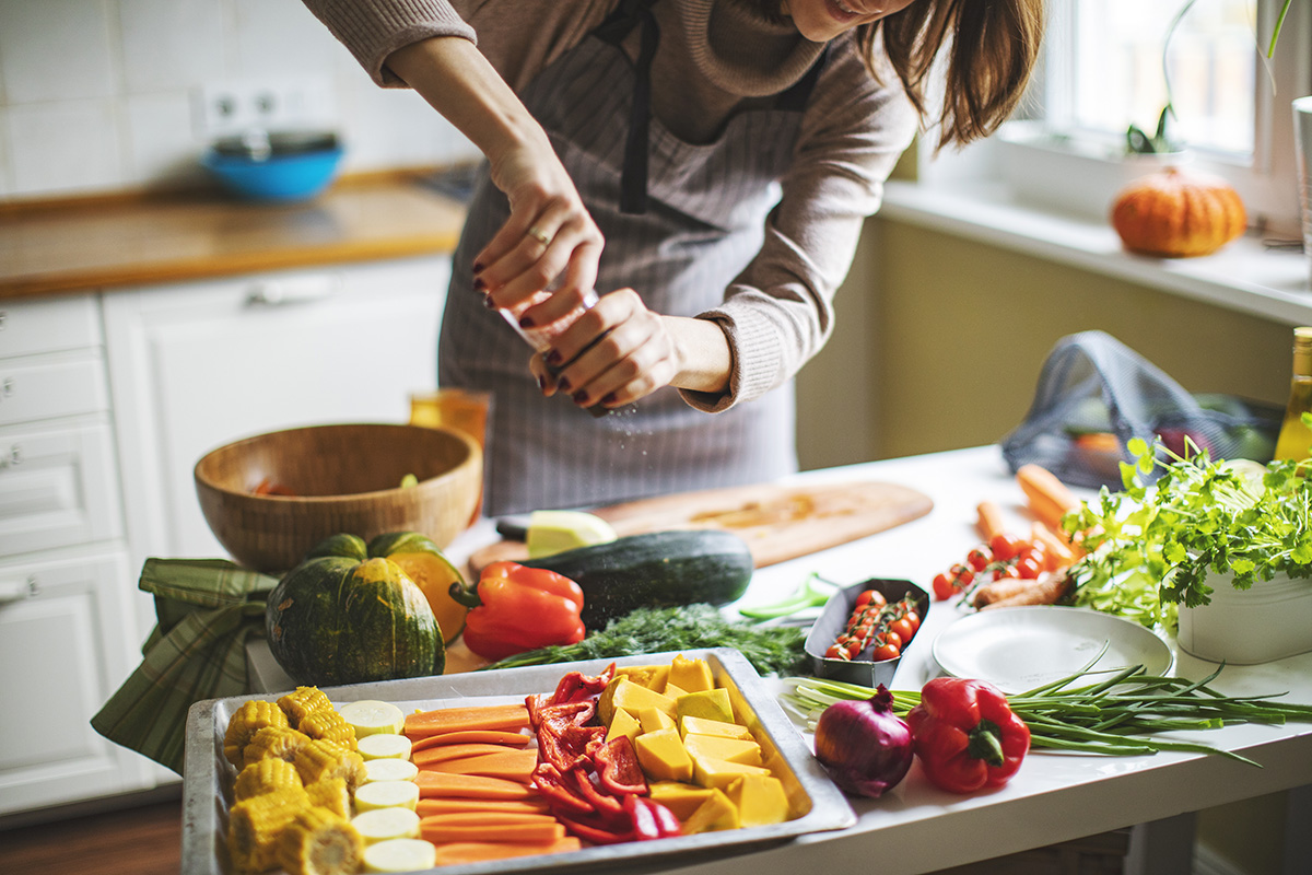 A woman seasoning raw vegetables on a baking tray