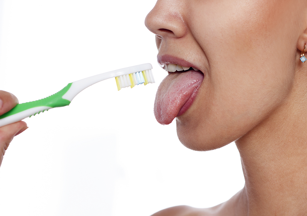 Close up of a woman about to brush her tongue with a toothbrush.