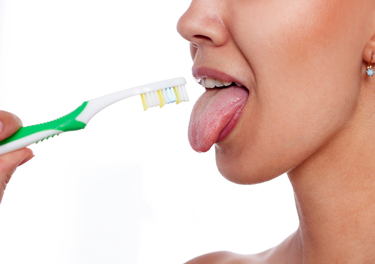 Close up of a woman about to brush her tongue with a toothbrush.