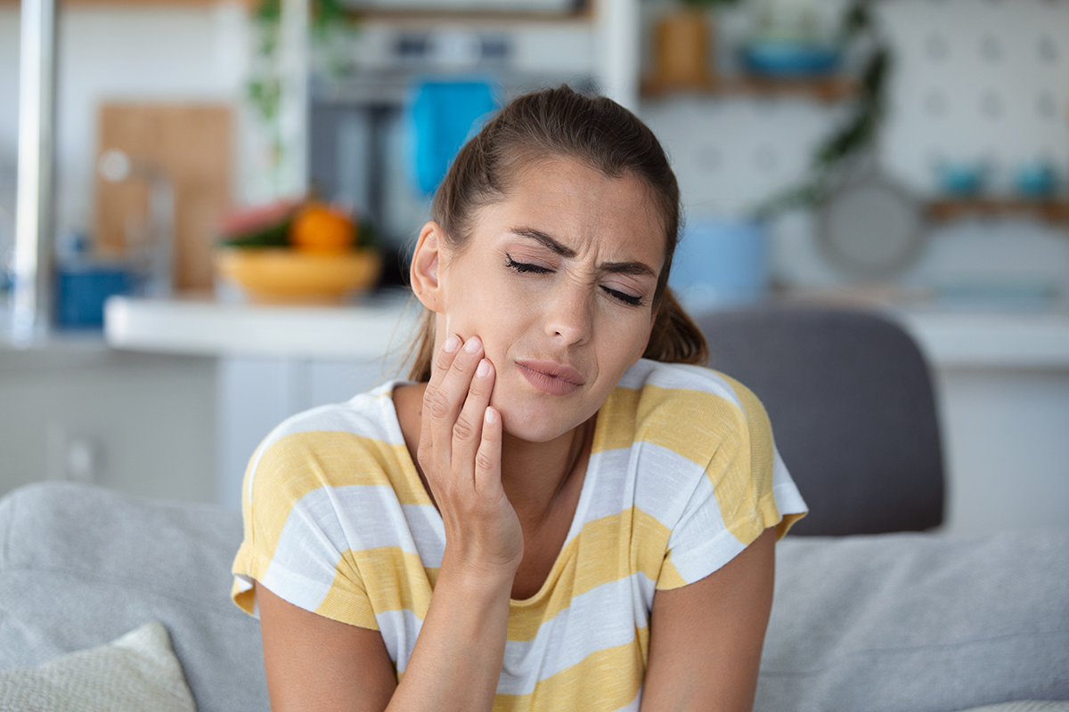A woman is touching her jaw with her hand, indicating that she is suffering from toothache.