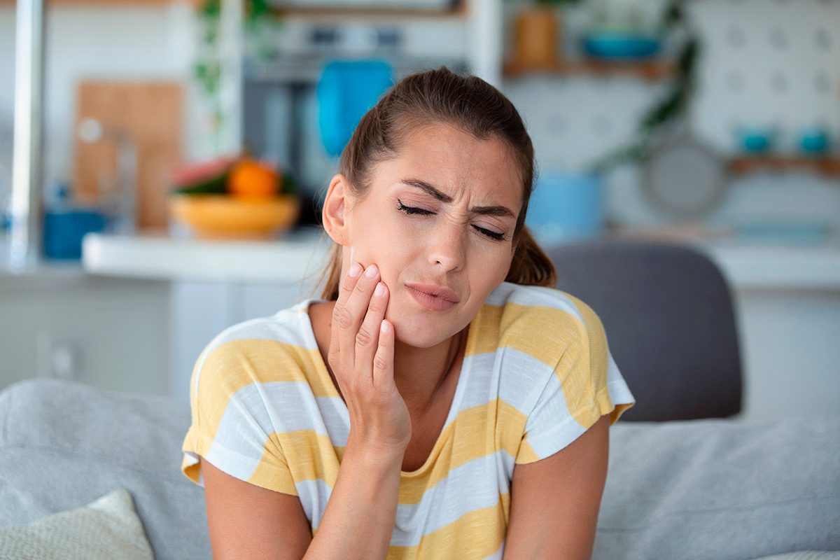 A woman is touching her jaw with her hand, indicating that she is suffering from toothache.