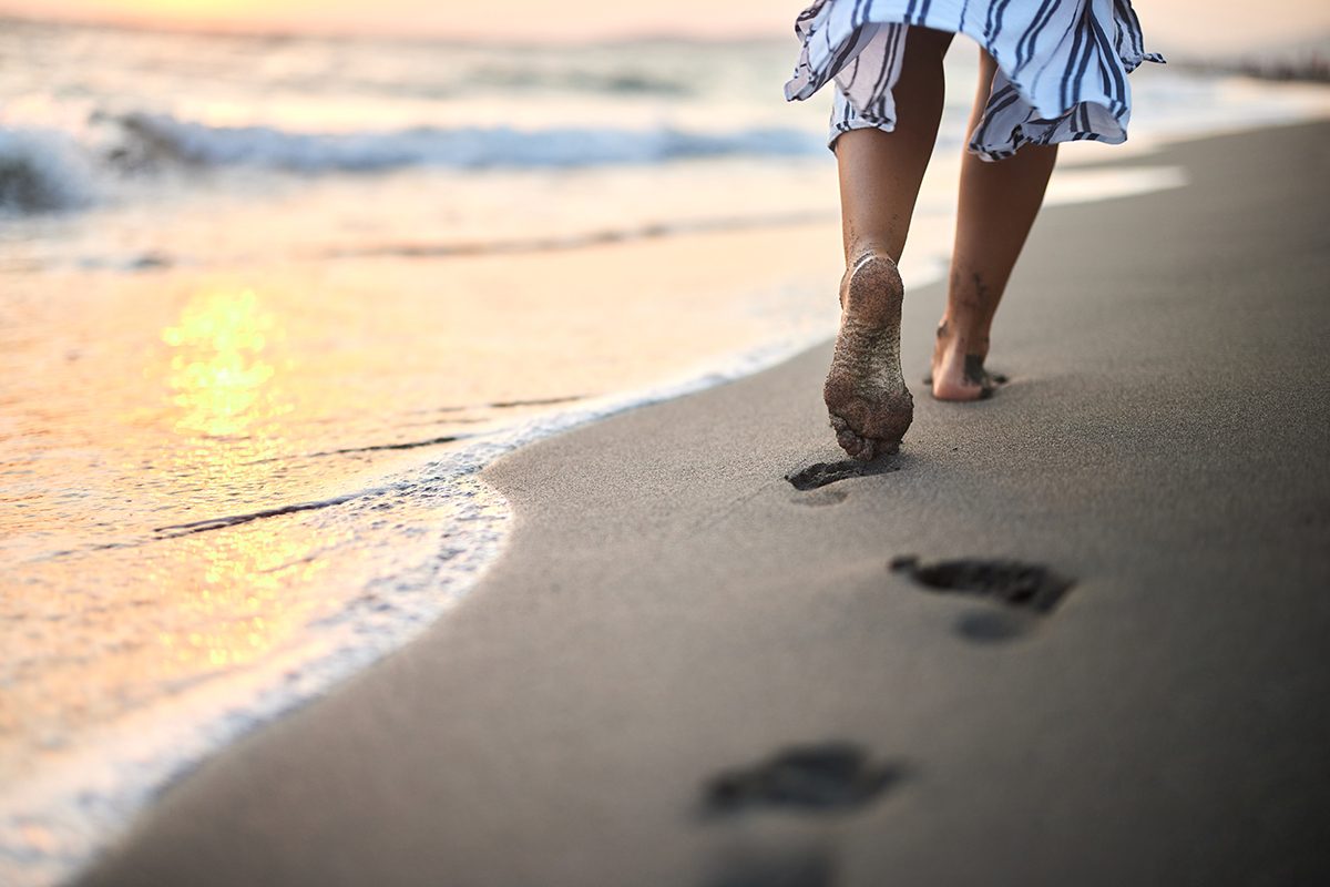A person walks barefoot on a beach, leaving footprints in the sand.